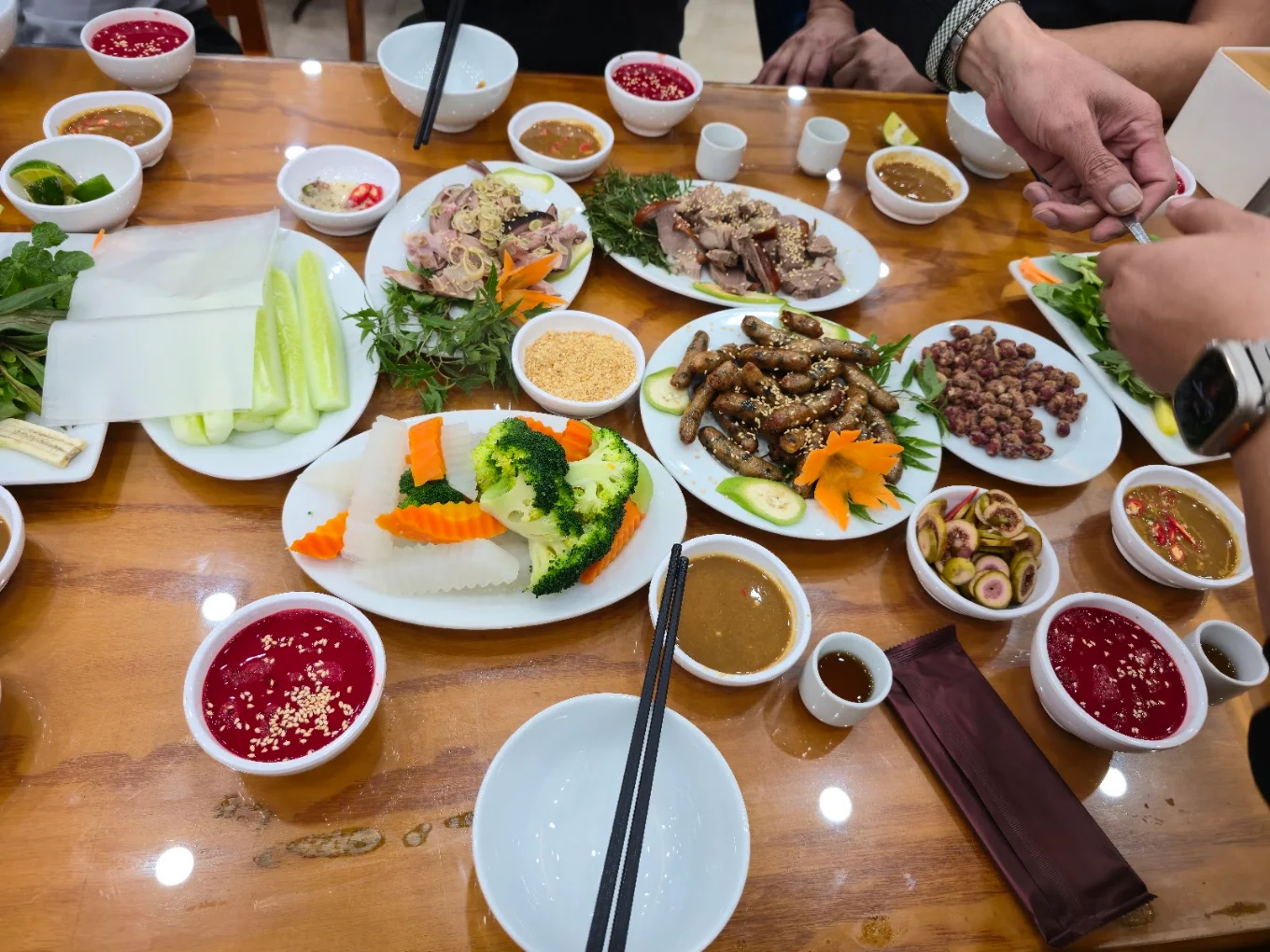 Bàn tiệc hấp dẫn với bát tiết canh dê đỏ tươi, dê tái chanh ăn kèm bánh đa nem và rau sống tươi sạch.