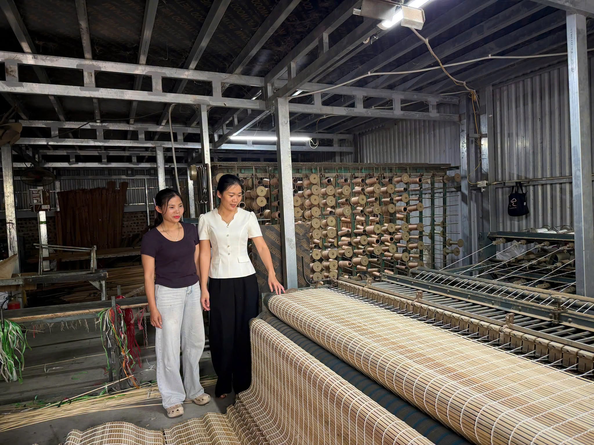 Người dẫn chương trình cùng thợ lành nghề giới thiệu hệ thống giàn dệt và các cuộn nan mành trúc thô mộc tại xưởng.