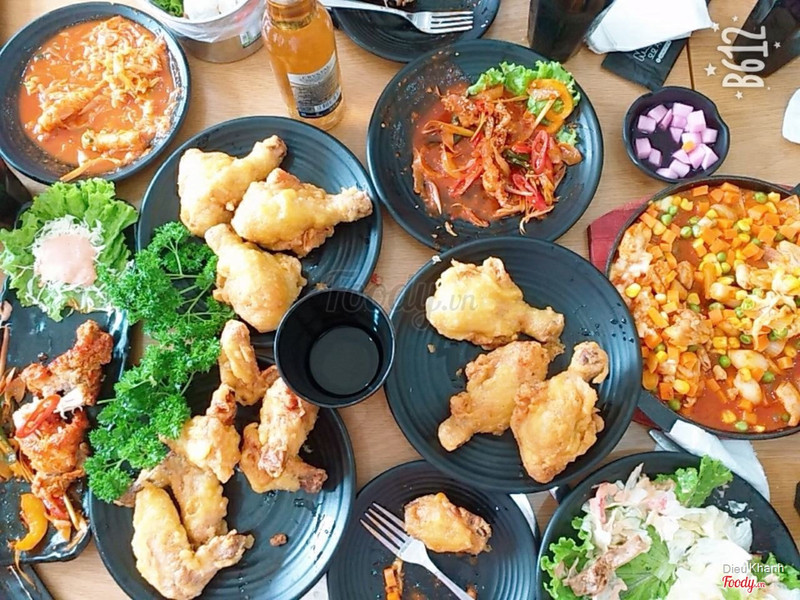 Bàn tiệc đa dạng sắc màu với các món gà chiên, salad tươi mát và panchan ăn kèm.