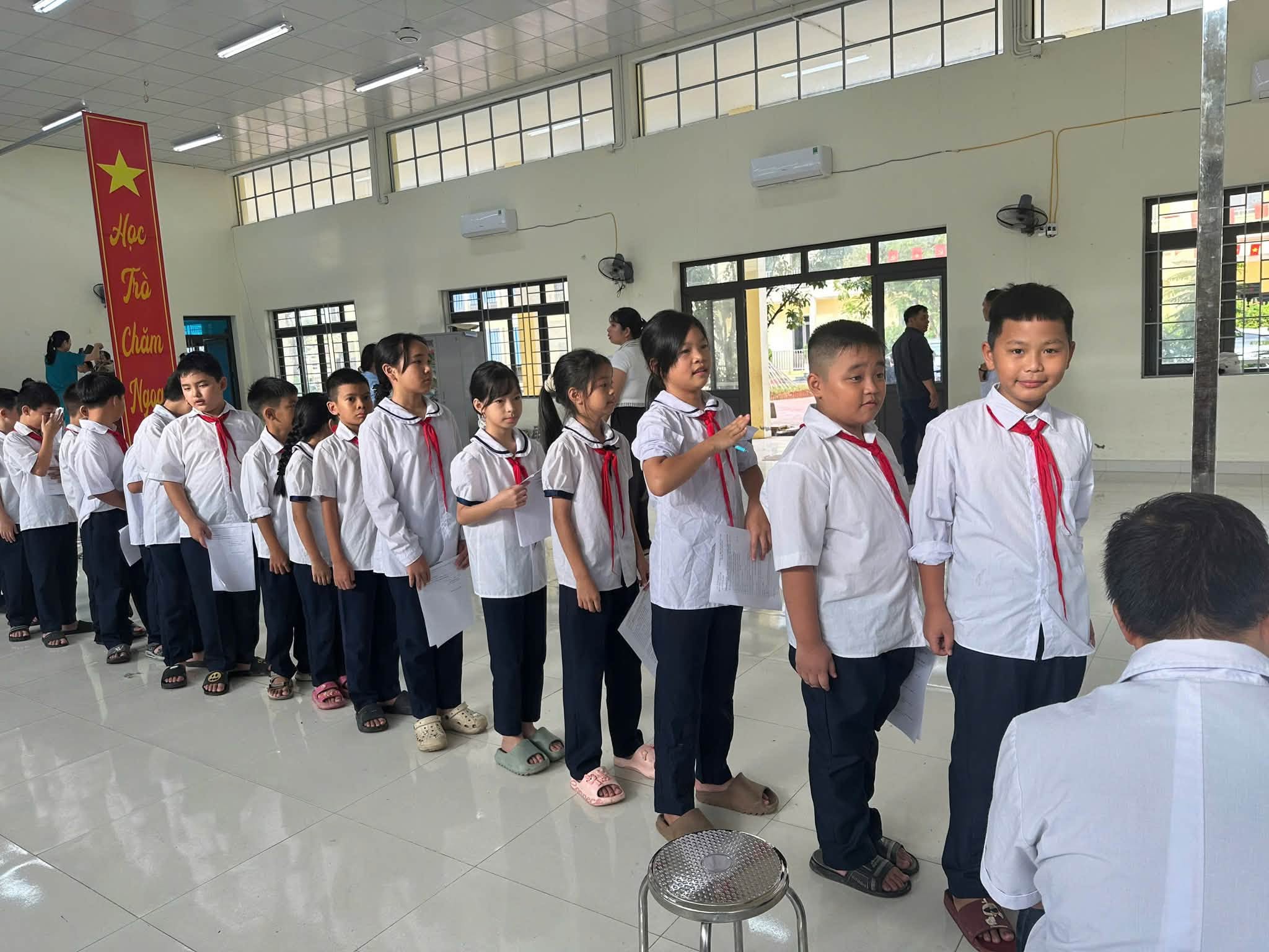 Hàng ngũ học sinh ngay ngắn, trật tự cầm trên tay phiếu theo dõi sức khỏe cá nhân.
