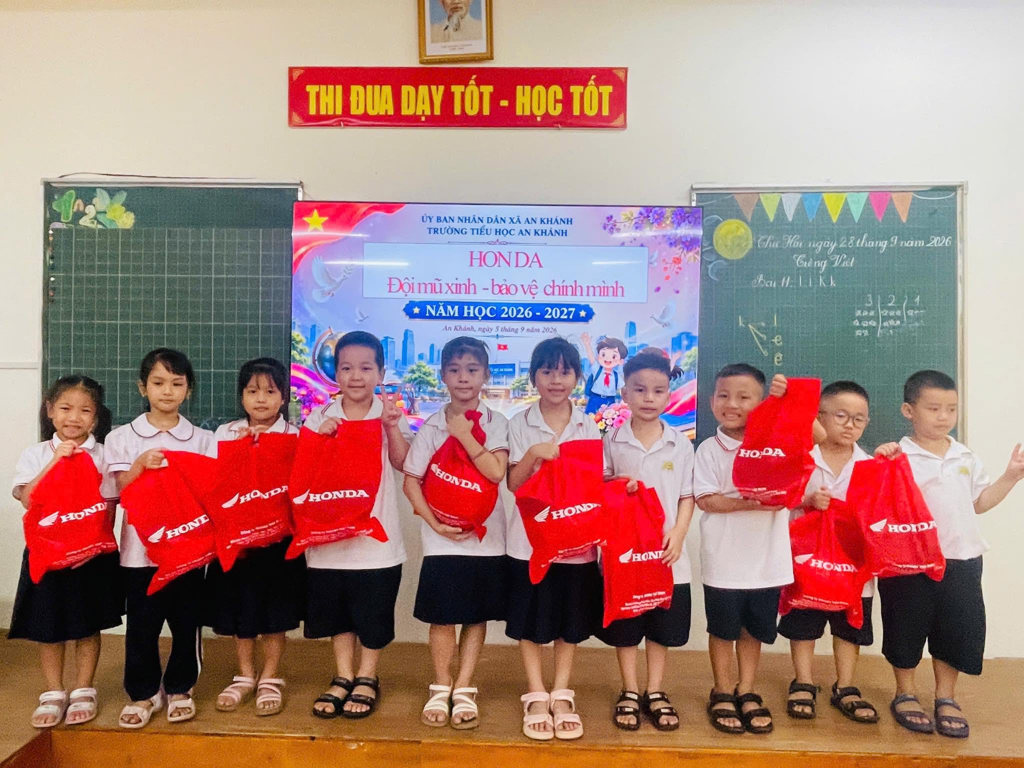 Các em học sinh ngoan ngoãn xếp hàng nâng niu chiếc túi đỏ đựng mũ bảo hiểm mới.